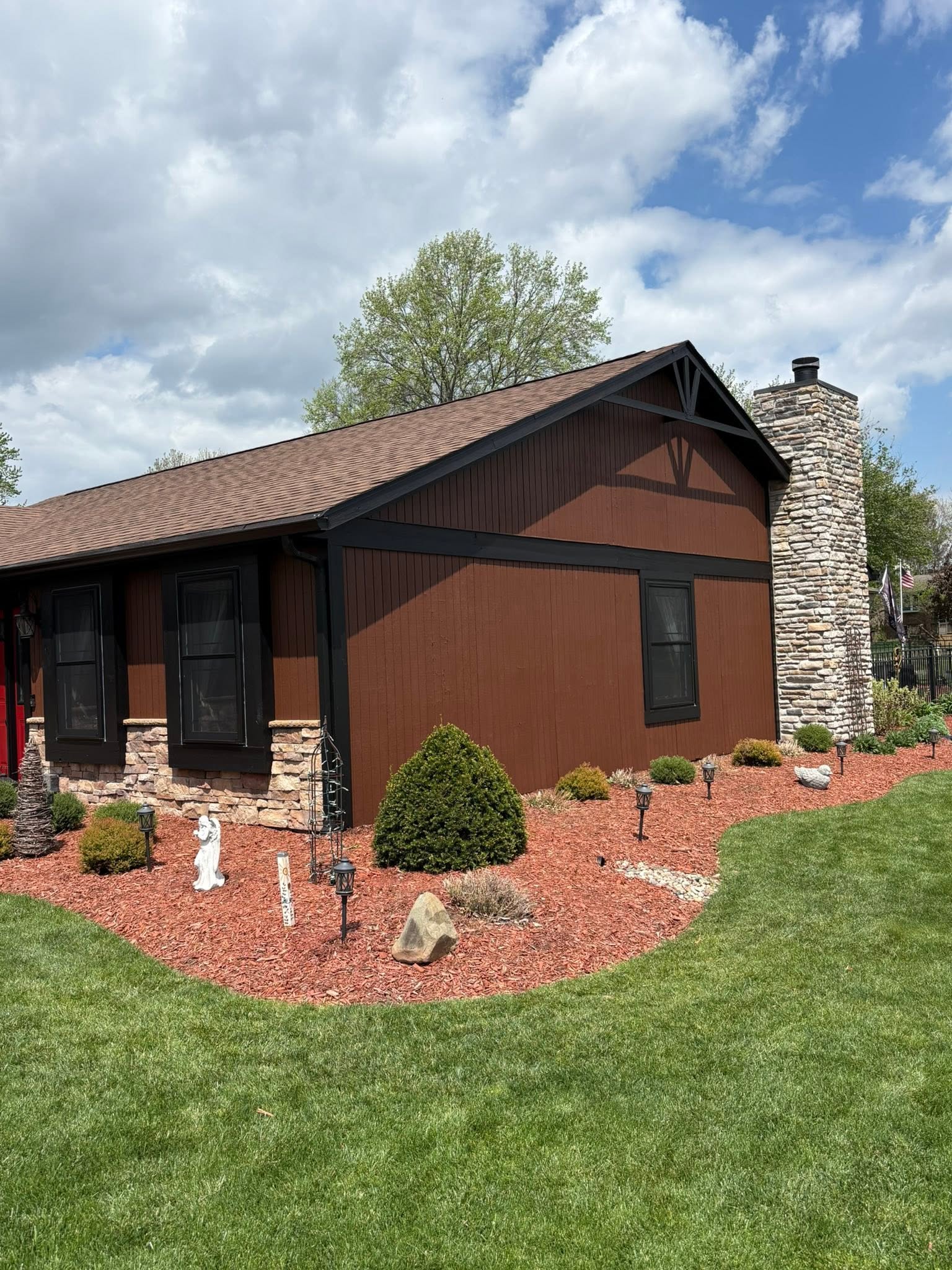 A freshly painted brown and black home exterior in a landscaped yard